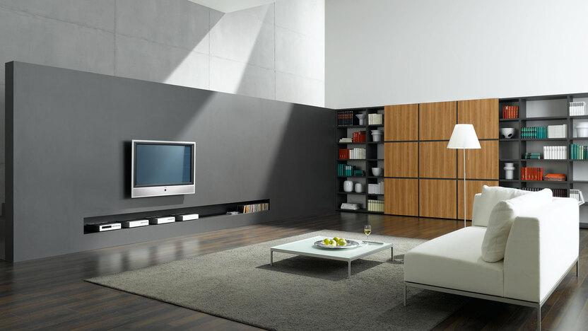 Offene Wohnraumimpression mit grauer TV-Trennwand zur Treppe und Einbauregal aus Holz und weißem Sofa